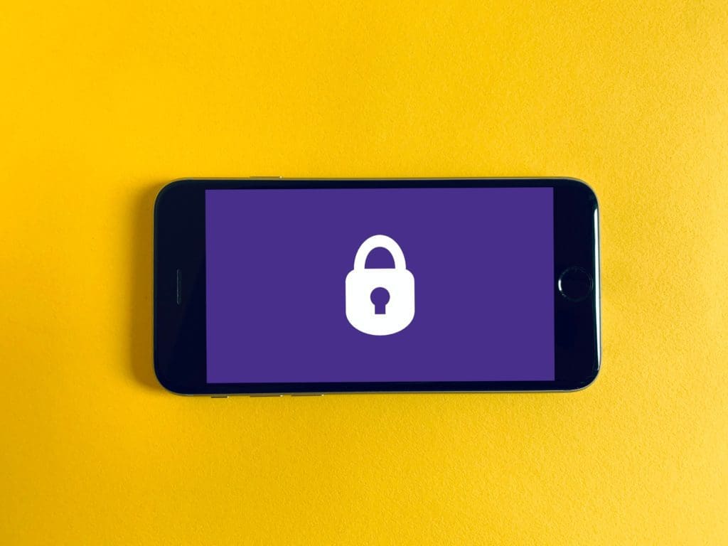 A smartphone on a bright yellow background. It has a purple screen with a white lock in the center.