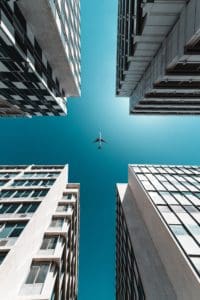 A plane flies directly above buildings. View from the ground.