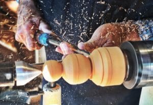 A woodworker sanding down a piece of decorative wood to their desired shape.