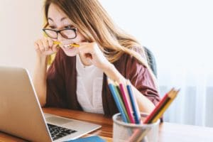 A woman sitting front of her computer biting a pencil in frustration, which is how Trade Promotion Management can feel. 